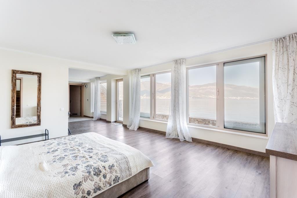 Bedroom with panoramic sea and mountain views in a villa, Krašići, Montenegro: bright interior, double bed, and mirror.