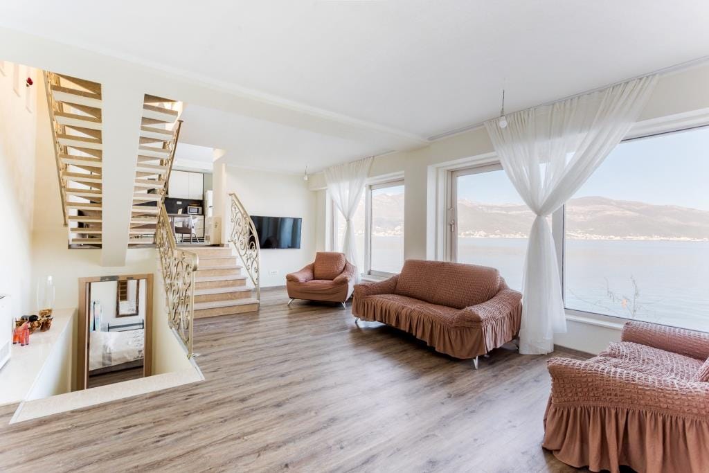 Living room with brown sofas, staircase, and large window overlooking water.