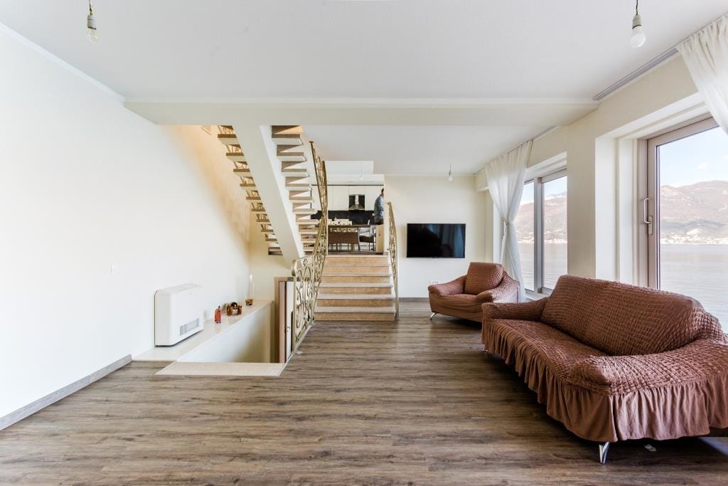 Villa living room in Krašići, Montenegro: panoramic sea view, staircase with wrought-iron railings, and soft seating.