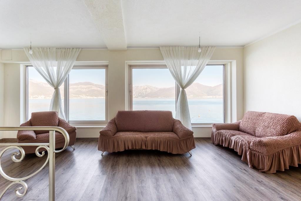Living room in a villa in Krašići, Montenegro: upholstered furniture with covers and panoramic sea and mountain views from the windows.