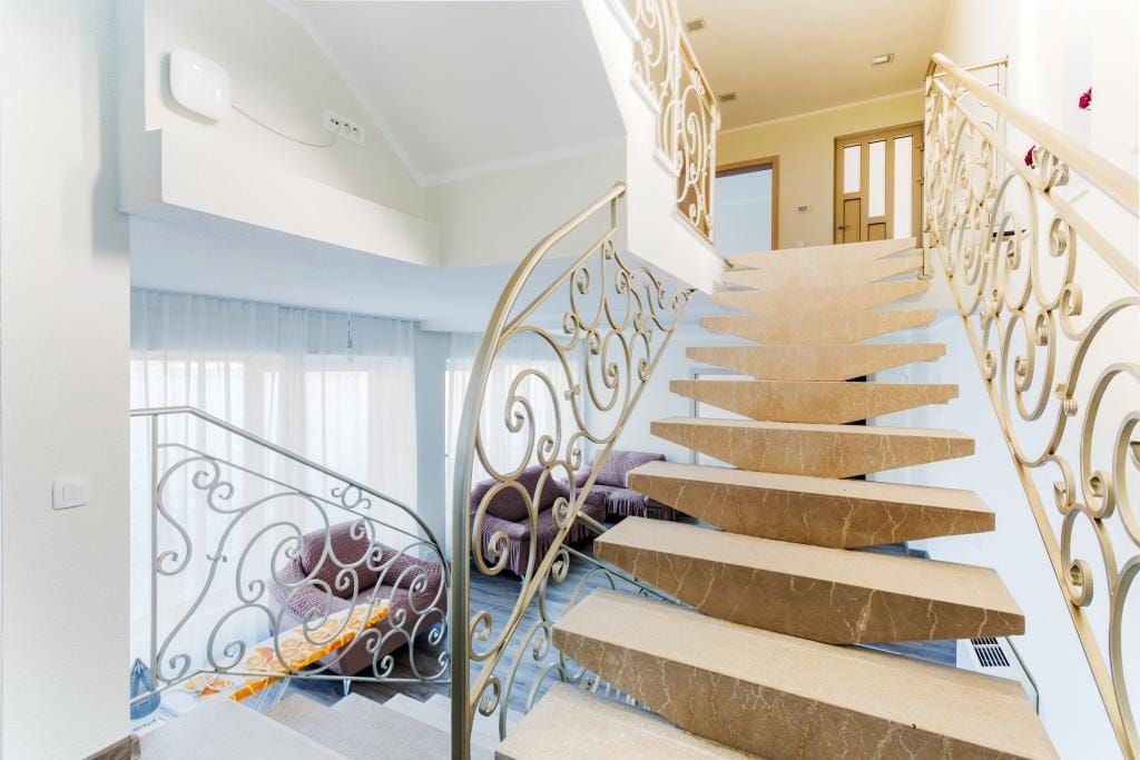 Marble staircase with wrought-iron railings in the interior of a villa in Krašići, Montenegro, view of the living room with upholstered furniture.