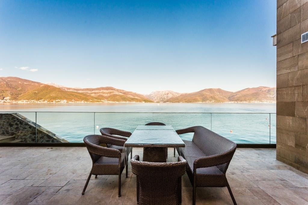 Villa terrace in Krašići, Montenegro: wicker furniture, glass railing, and panoramic sea and mountain views.