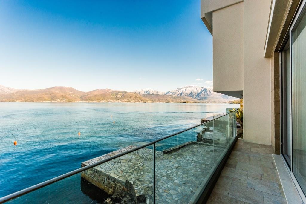 Balcony with glass railing overlooking a lake and mountains.