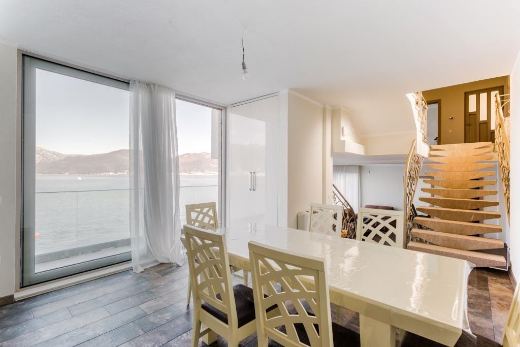 Living room with dining area and panoramic sea view in a villa, Krašići, Montenegro: light furniture and staircase.