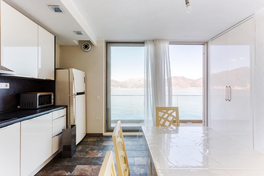 Modern kitchen with sea view in a villa, Krašići, Montenegro: white furniture, dining area, and panoramic windows.