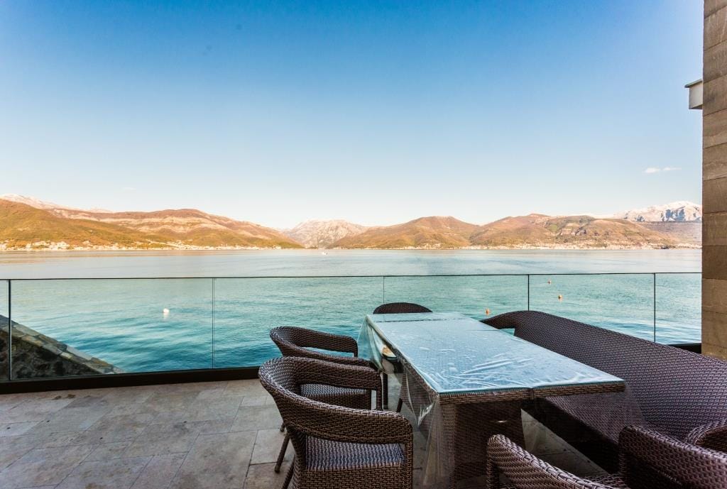 Villa terrace in Krašići, Montenegro: wicker furniture, glass railing, and panoramic sea and mountain views.