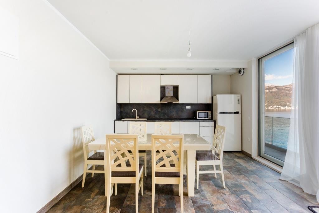 Modern kitchen-dining room in a villa in Krašići, Montenegro, with panoramic sea and mountain views through the balcony.