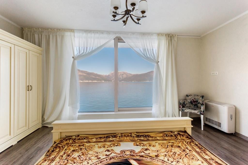 Bedroom with panoramic sea and mountain views in a villa, Krašići, Montenegro: light furniture, parquet flooring, and classic decor.