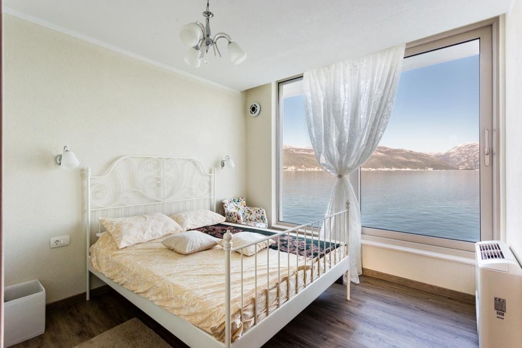Bedroom with panoramic sea and mountain views in a villa, Krasici, Montenegro: white wrought-iron bed and bright interior.
