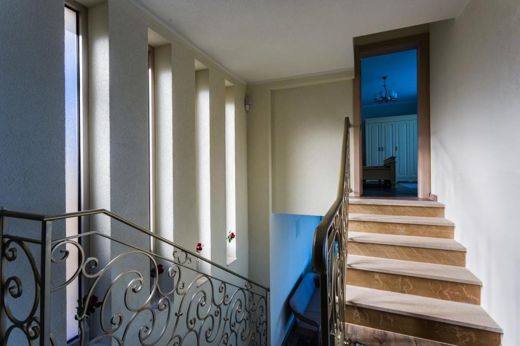 Staircase with ornate metal railing and narrow vertical windows leading to a doorway into a blue room.