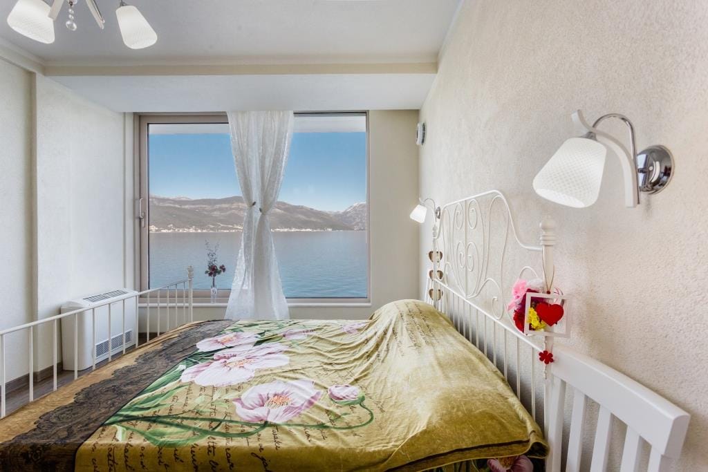 Bedroom with panoramic sea and mountain views in a villa, Krasici, Montenegro: white wrought-iron bed and bright interior.