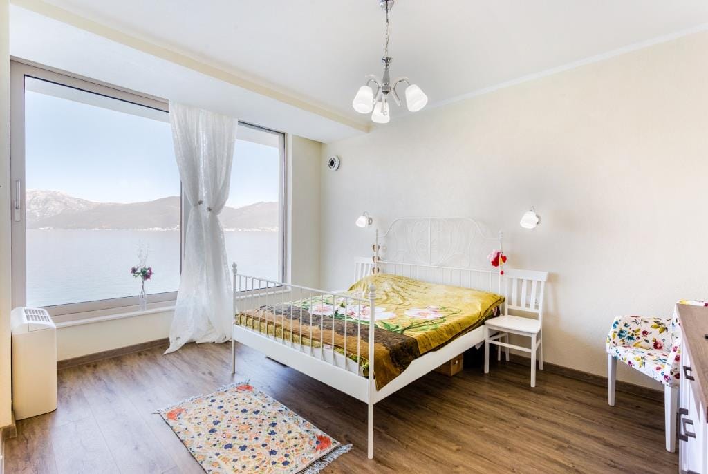Bedroom with panoramic sea and mountain views in a villa in Krašići, Montenegro: white bed, laminate flooring, and a bright interior.