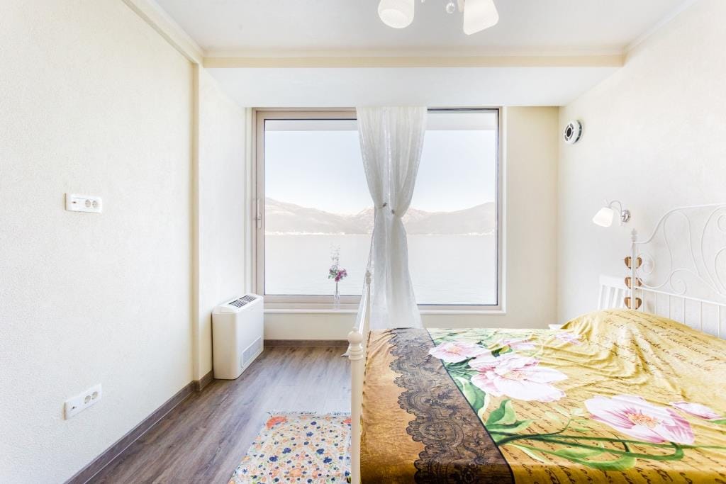 Bright bedroom with sea view in a villa, Krašići, Montenegro: double bed, panoramic window, and laminate flooring.