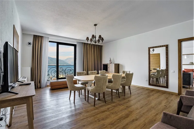 Living room with dining table, sofa, TV, and balcony offering a scenic lake view.