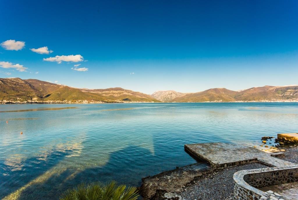 Panoramic view of the sea and mountains from the villa’s private beach in Krašići, Montenegro, with a stone pier by the water.
