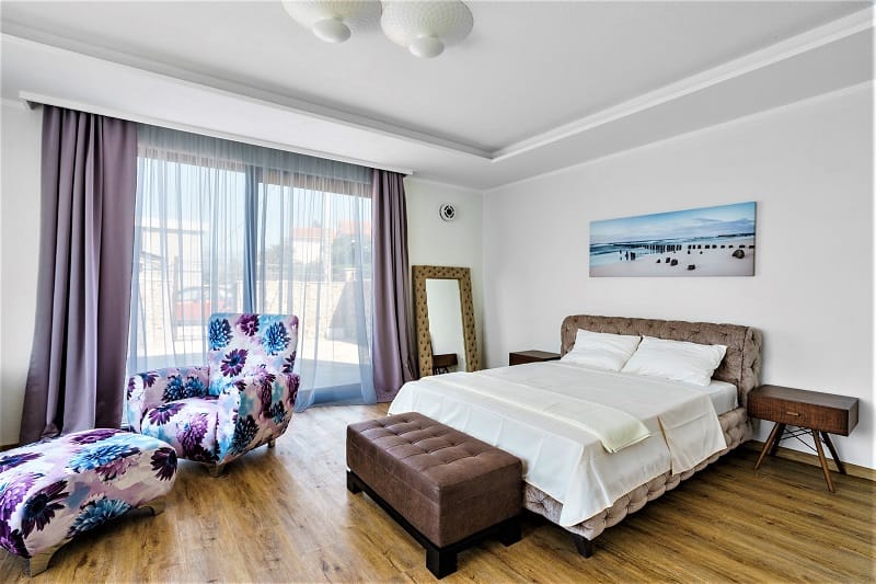 Modern bedroom with a double bed and a bright armchair in a villa in Krašići, Montenegro, with access to the terrace.