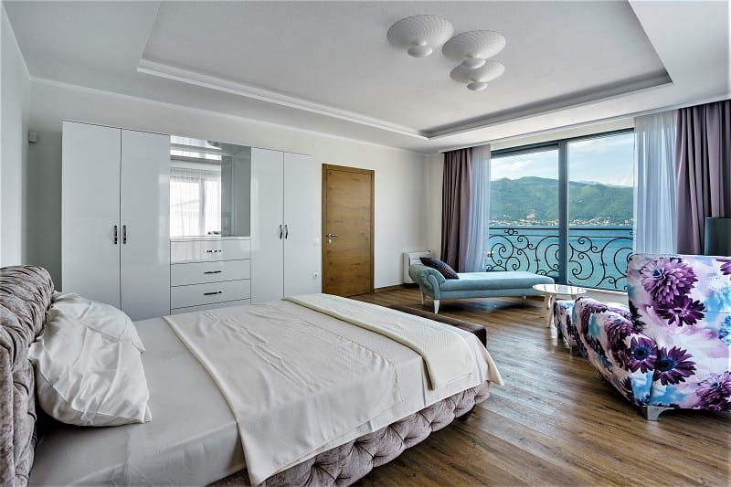 Bedroom in a villa in Krašići, Montenegro: double bed, white wardrobe, sea and mountain views through panoramic windows.