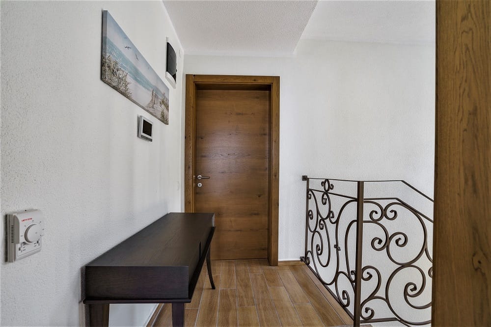 Bright villa hallway in Krašići, Montenegro: wooden door, wrought-iron staircase railing, and a console table.