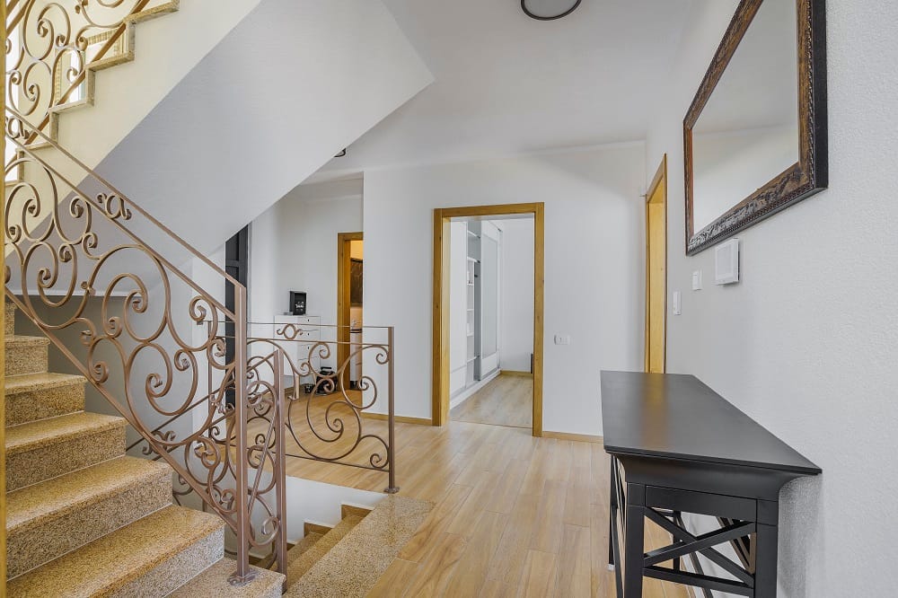 Interior of a villa in Krašići, Montenegro: a stone staircase with wrought-iron railings, light finishes, and a black console.