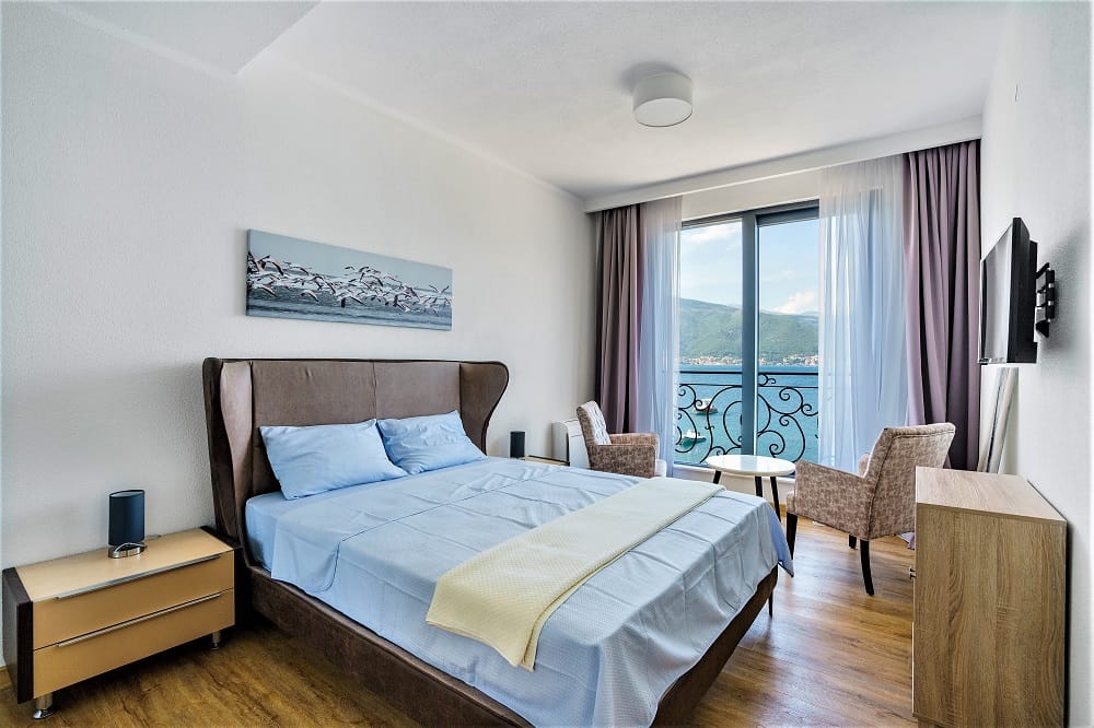 Bedroom in a villa in Krašići, Montenegro: double bed, panoramic sea and mountain view, balcony with wrought iron railing.