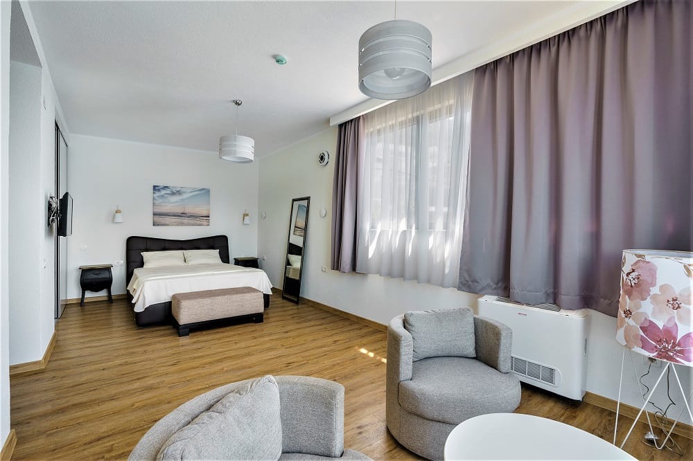 Bright bedroom with a double bed and sitting area in a villa in Krašići, Montenegro, with parquet flooring and panoramic windows...