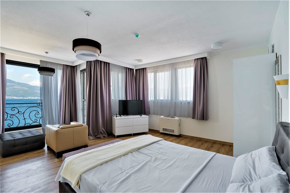 Bedroom with sea view in a villa in Krašići, Montenegro: double bed, TV, armchair, and a balcony with a panoramic view.