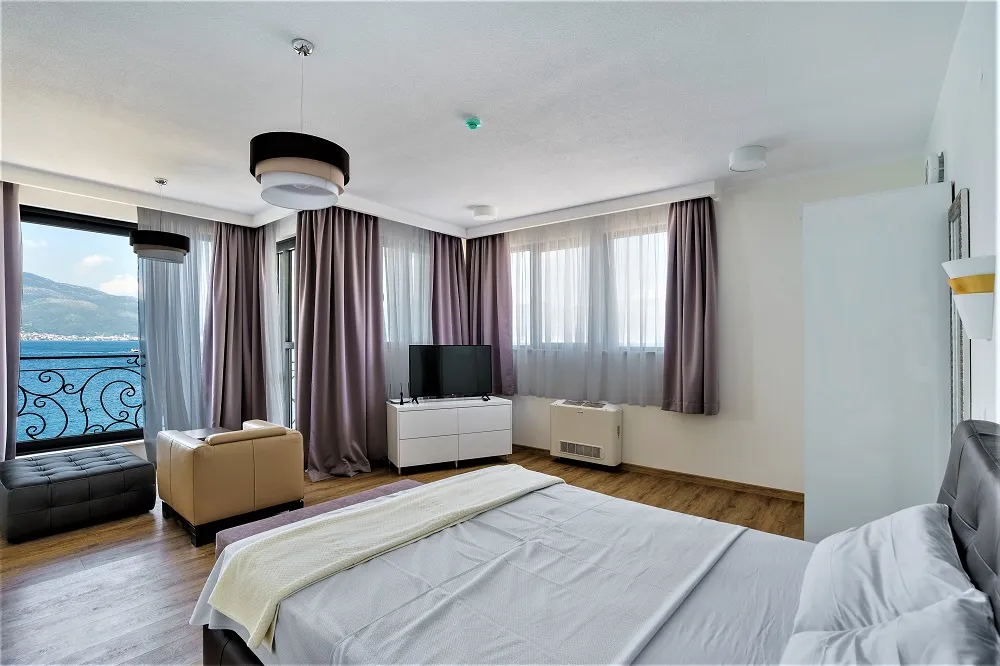 Bedroom featuring a large bed, TV on a white dresser, tan leather chair, and a balcony with sea views.