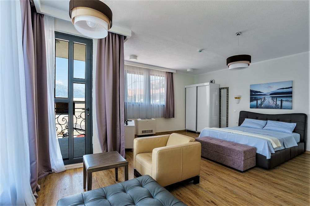 Modern bedroom in a villa in Krašići, Montenegro: double bed, armchair, balcony with a view, and stylish interior.