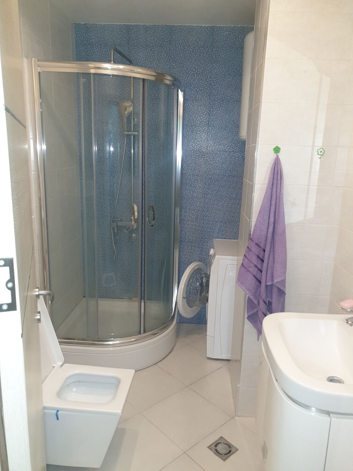 Bathroom in an apartment in Budva, Montenegro: shower cabin, washing machine, sink, and light-colored tiles.