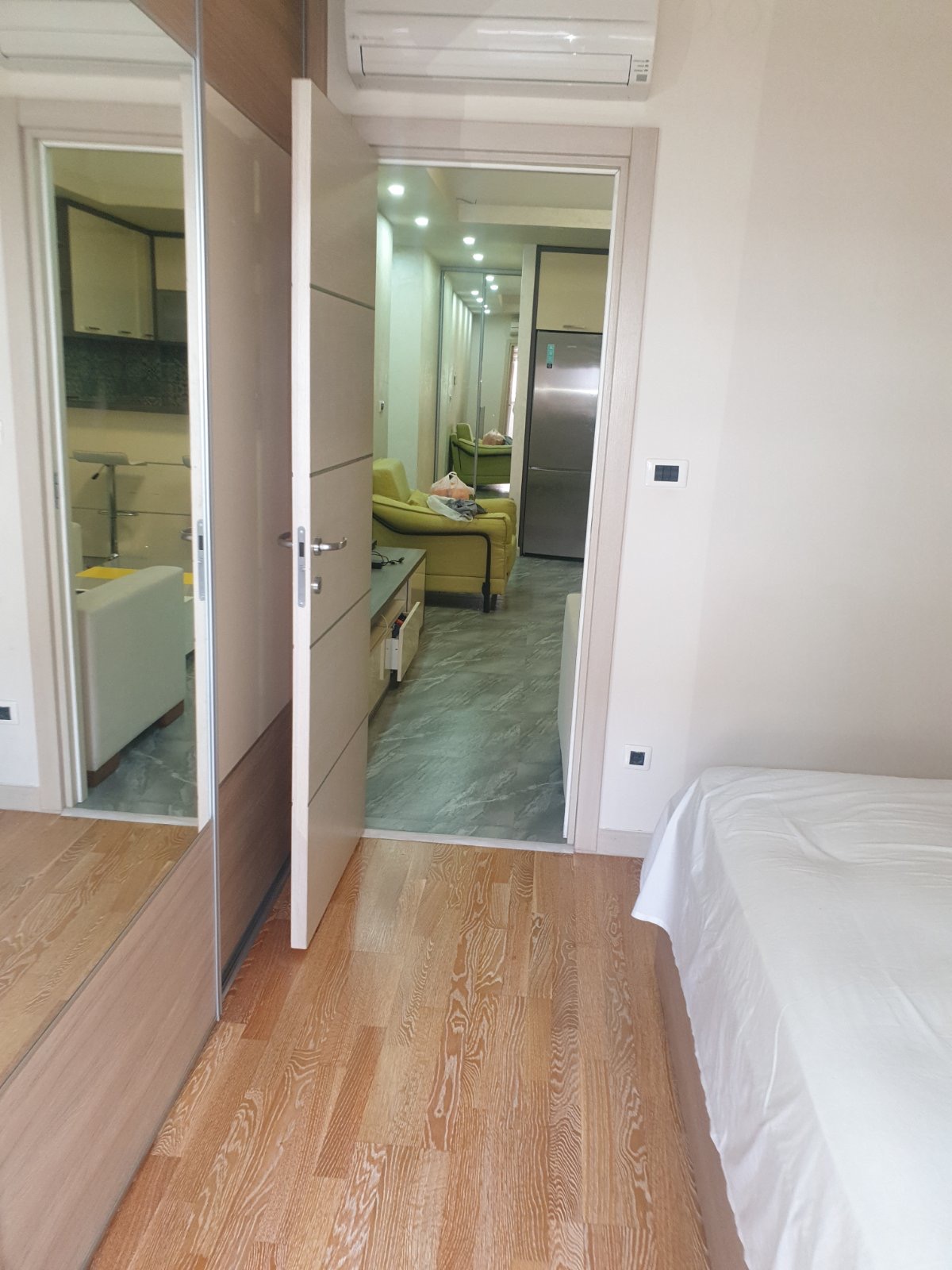 Bedroom with a mirrored wardrobe and a view of the living room in an apartment in Budva, Montenegro: modern interior and parquet flooring.