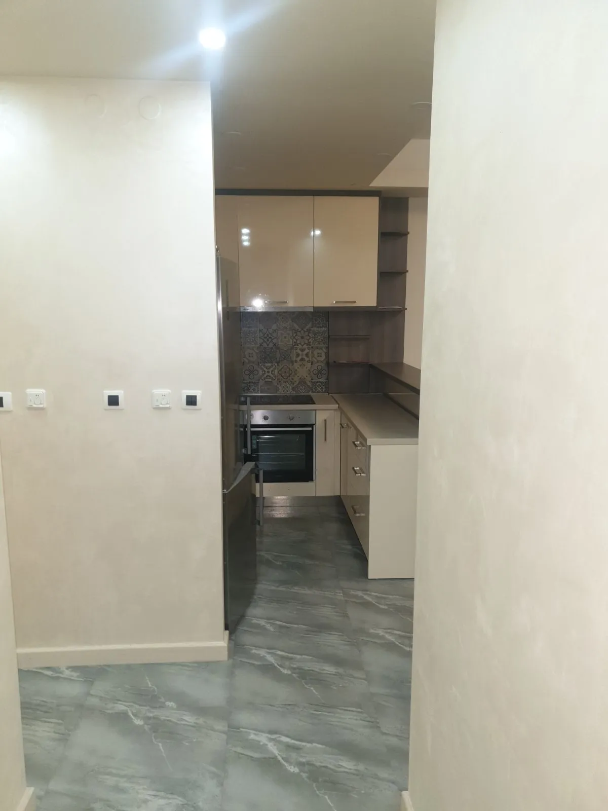 View of a kitchen through a doorway featuring light cabinets, a built-in oven, refrigerator, and decorative backsplash tiles.