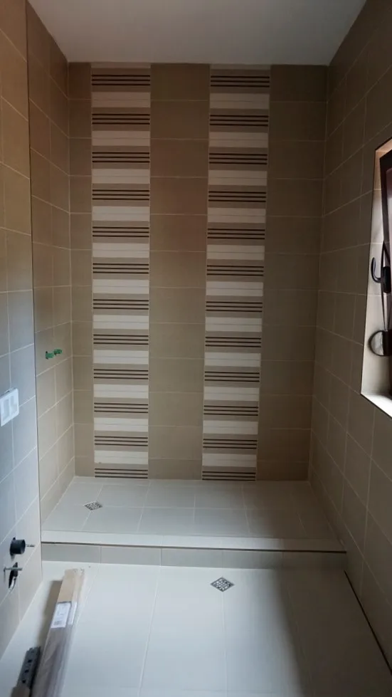 Tiled shower area with decorative striped wall, two floor drains, and unfinished plumbing fixtures.