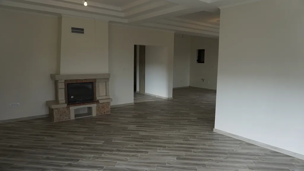 Empty room featuring a stone fireplace and wood-look tile flooring. White walls and coffered ceiling beams are visible.