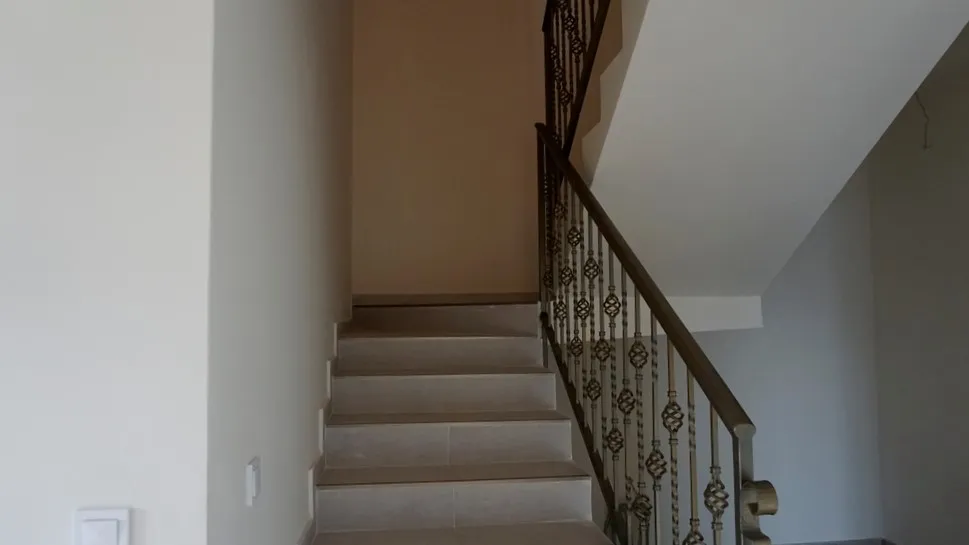 Interior staircase with beige tiled steps and a metal railing featuring decorative ornamental balusters.