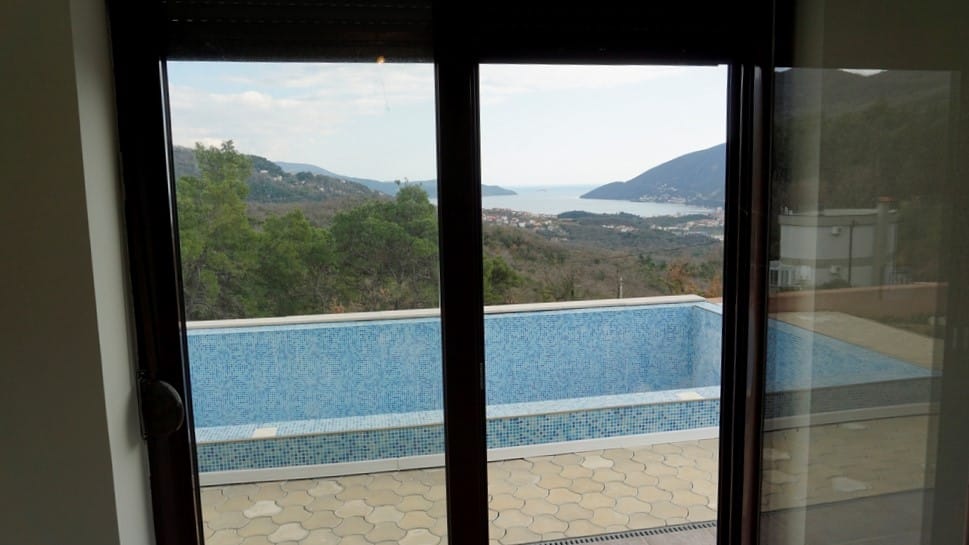 View from the villa window in Igalo, Montenegro: a mosaic-tiled pool, terrace, and panoramic sea and mountain views.