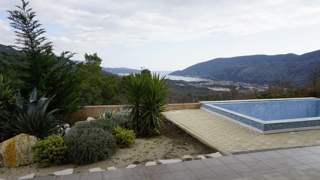 Outdoor pool at a villa in Igalo, Montenegro, with panoramic views of the mountains and Kotor Bay, landscaped grounds.