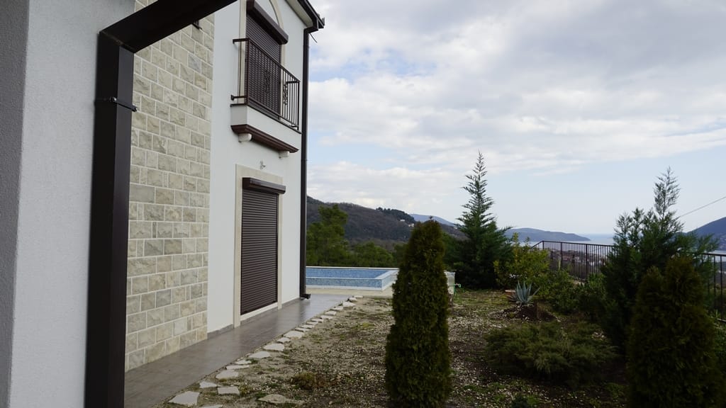Villa facade in Igalo, Montenegro: stone cladding, pool, garden, and panoramic sea and mountain views.