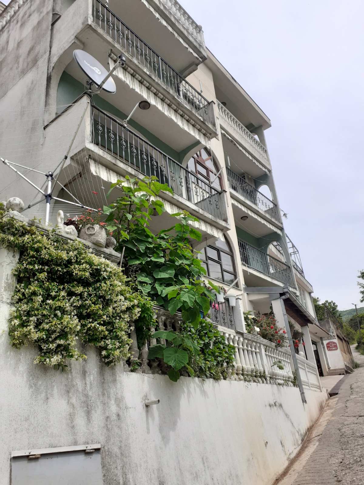 Facade of a mini-hotel in Zelenika, Herceg Novi, Montenegro: a multi-story building with balconies and a flowering garden at the entrance.