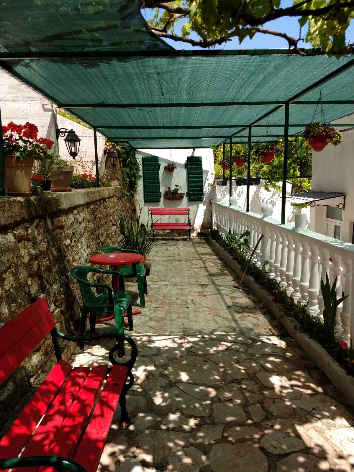 Cozy covered terrace with red benches at a mini-hotel, Zelenika, Herceg Novi, Montenegro. Stonework and garden.