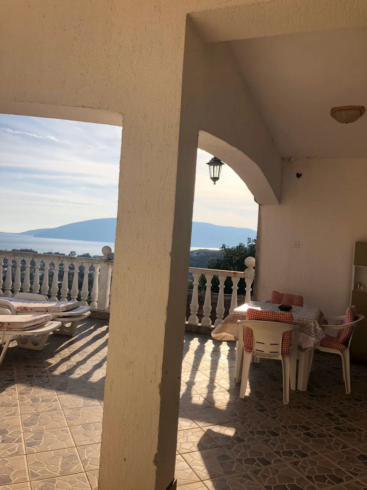 Terrace with white balustrade, plastic furniture, and a view of the sea and mountains.