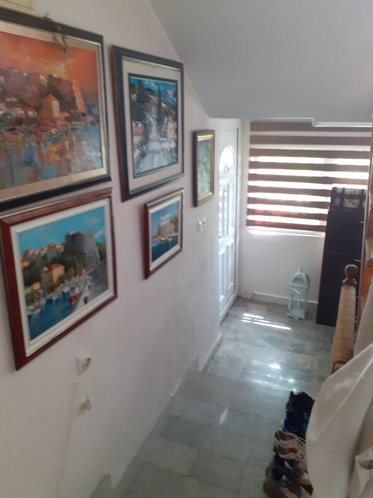 Staircase in the Zelenika mini-hotel, Herceg Novi, Montenegro: walls with paintings, stone floor, and an entrance door with shutters.
