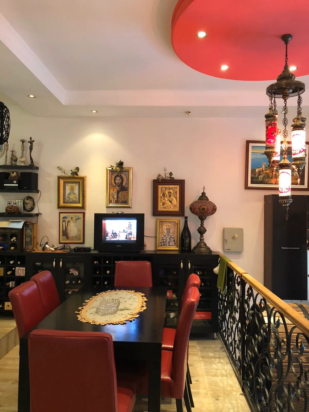 Dining area with a black table, red chairs, religious icons on the wall, a wine cabinet, and an ornate hanging lamp.