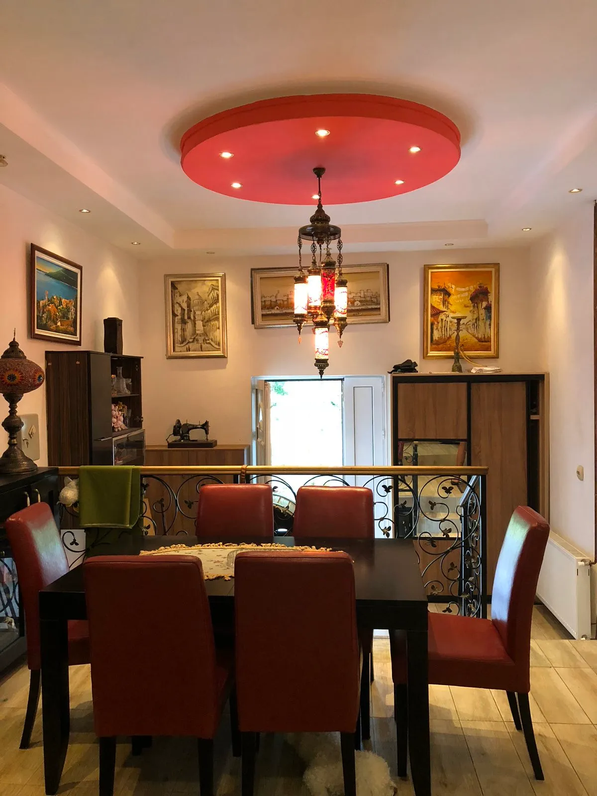 Dining area with a black table, red chairs, nautical wall art, and a decorative red ceiling medallion above.