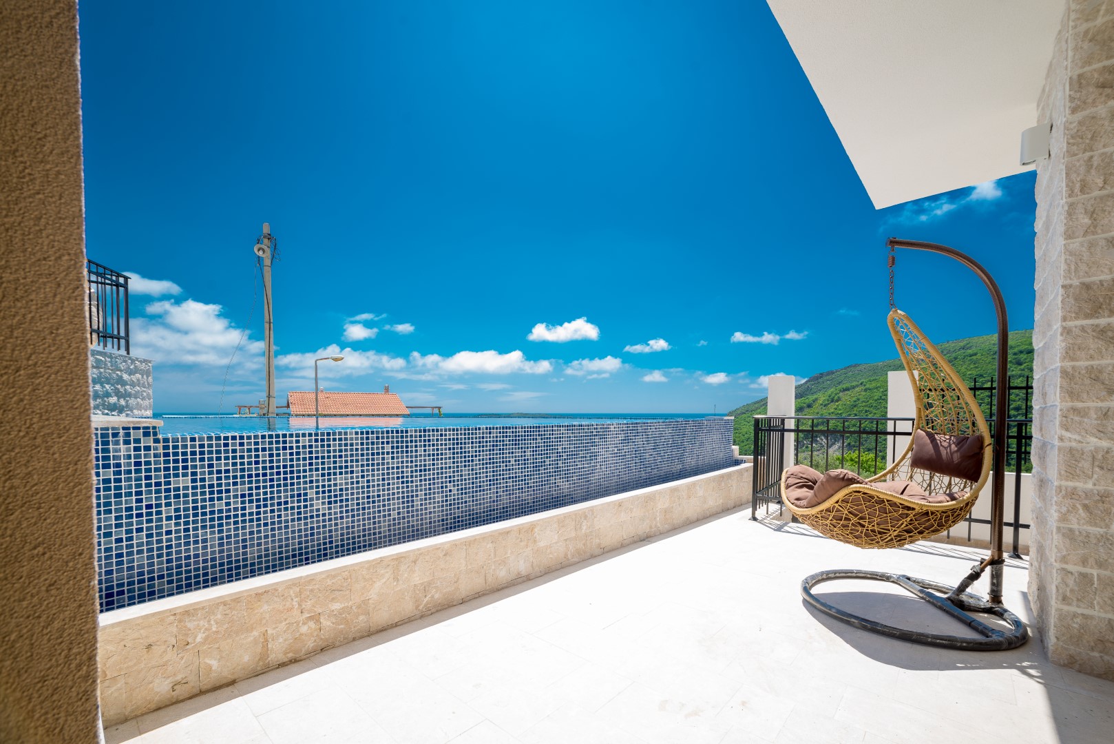Villa terrace in Bečići, Montenegro: infinity pool with blue mosaic, woven cocoon chair, and sea view.