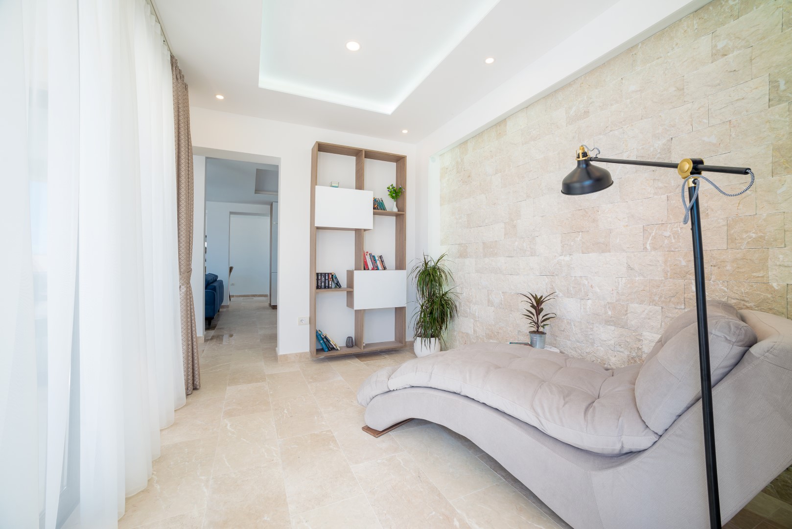 Living room in a villa in Bečići, Montenegro: a chaise lounge, shelving unit, and an accent wall of natural stone in the interior.