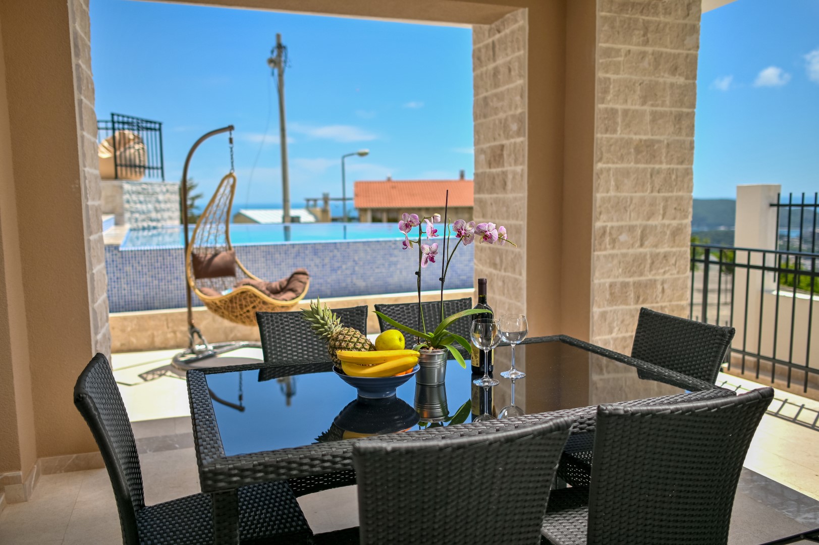 Villa terrace in Bečići, Montenegro: dining area, pool view, wicker cocoon chair, and sea view.