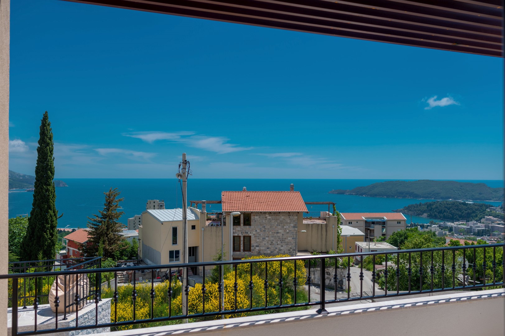 View from the villa balcony in Bečići, Montenegro: a panorama of the Adriatic Sea, mountains, and tiled house roofs.