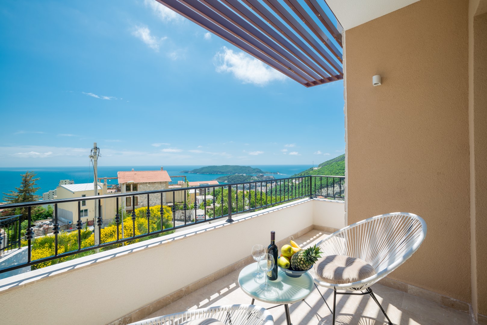Villa balcony in Bečići, Montenegro: panoramic sea view, wicker furniture, a table with wine and fruit.