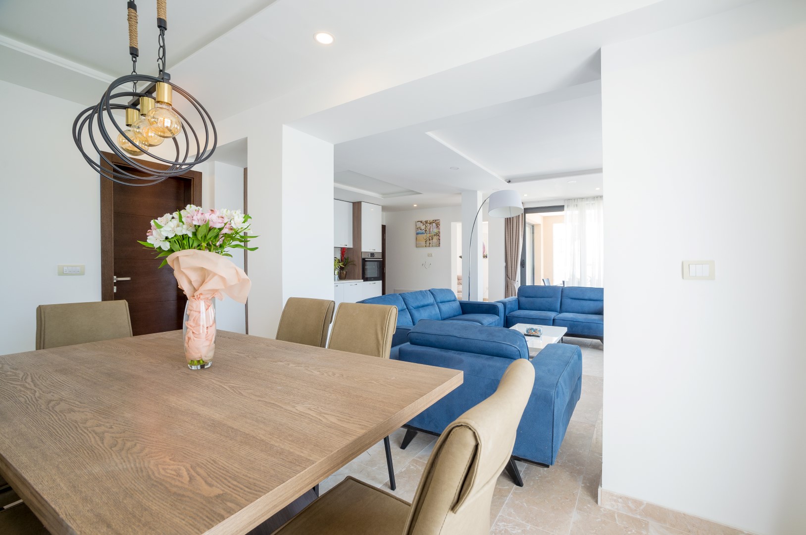 Modern living room with dining area in a villa in Bečići, Montenegro: wooden table, blue sofas, and a bright interior.