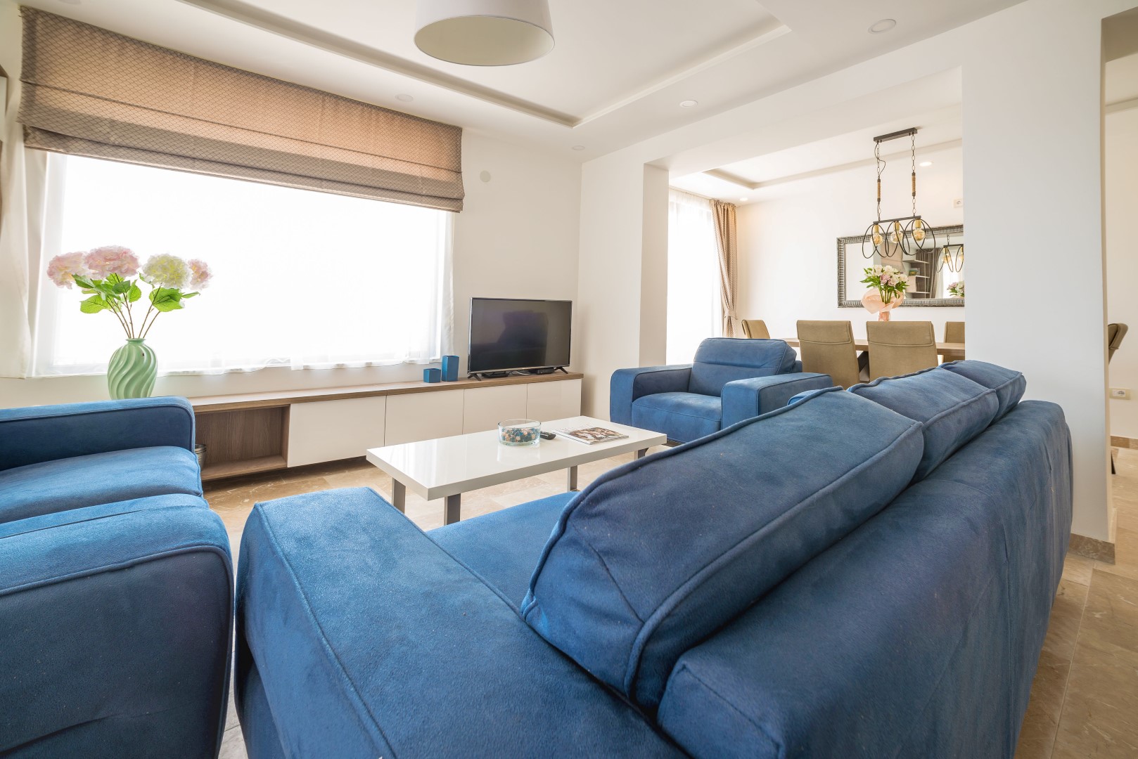 Bright living room with blue sofas in a villa in Bečići, Montenegro: modern interior, dining area, and TV area.